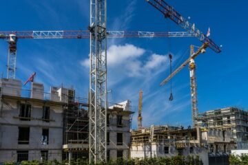 Precast high-rise building under construction with scaffold and tower crane under blue sky