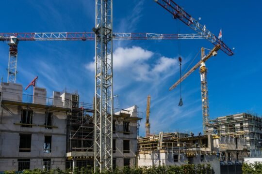 Precast high-rise building under construction with scaffold and tower crane under blue sky